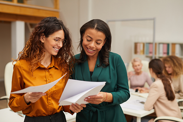 Women smiling, sharing information Background is a group of other women conversing