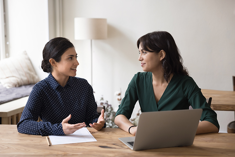 Two women talking, discussing over laptop and paper form